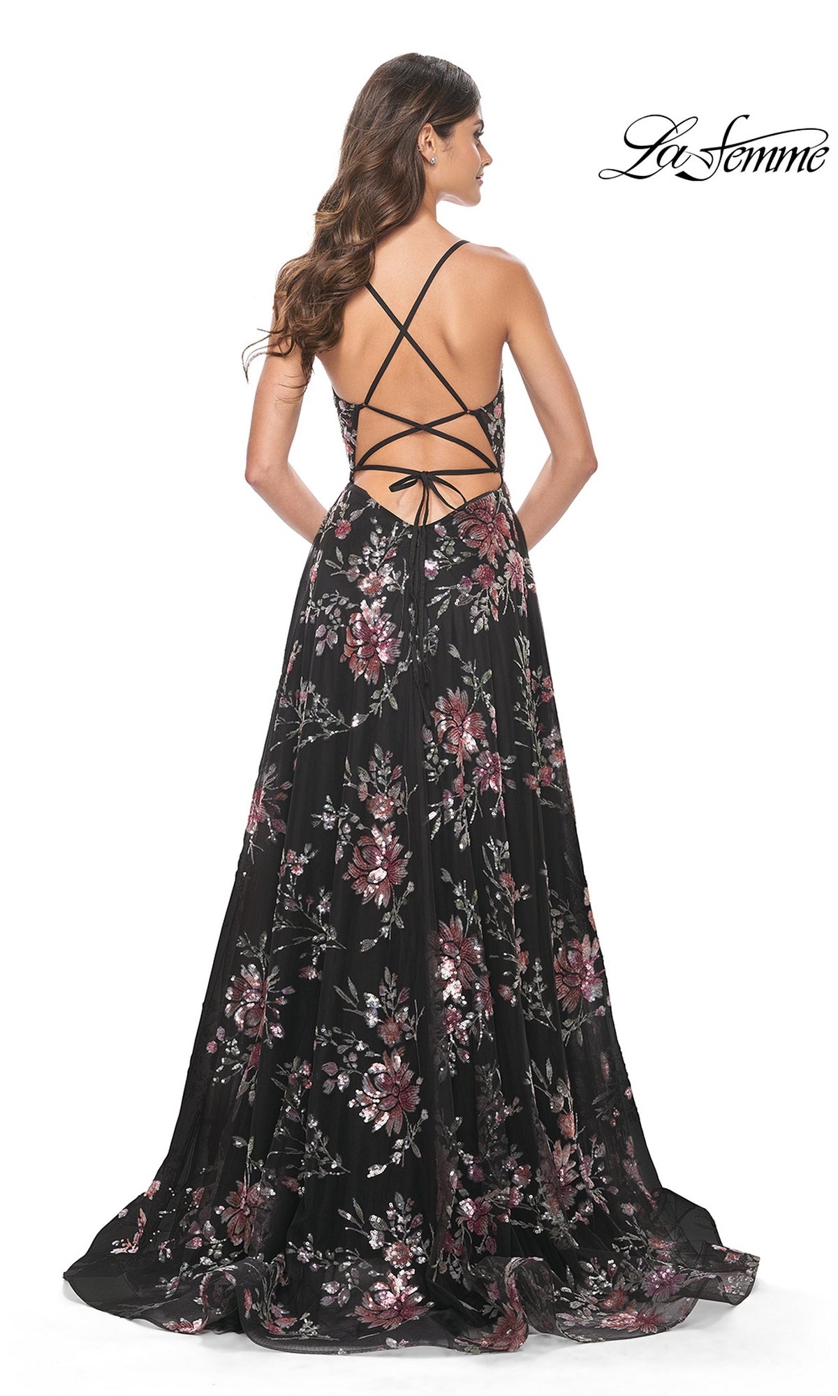 A woman stands facing away in the La Femme Floral-Sequin Long A-Line Prom Dress 32031, a black gown adorned with pink and purple floral sequins and an open crisscross back for an elegant prom look.